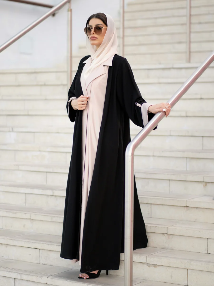 Woman in a black abaya over a blush dress on a stone staircase