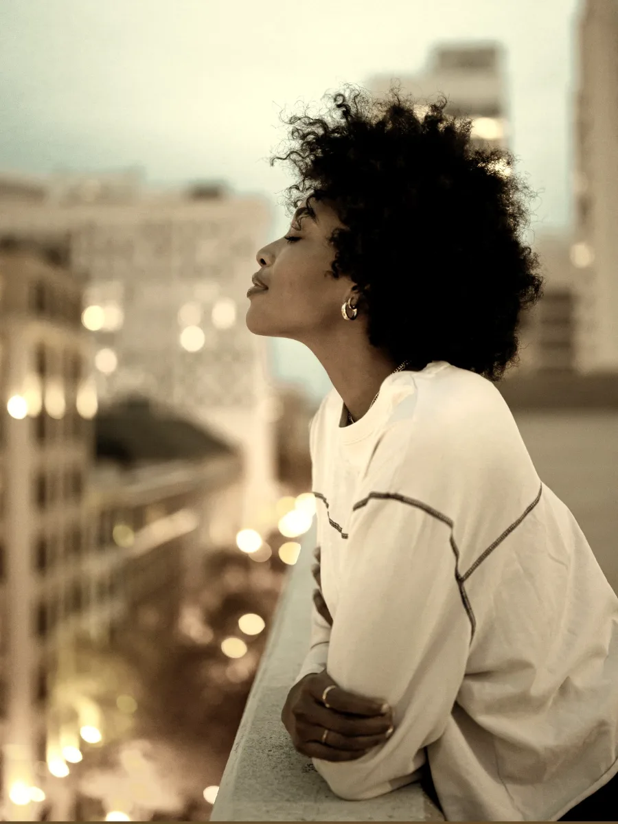 Woman in an oversized white long-sleeve top on a rooftop at dusk