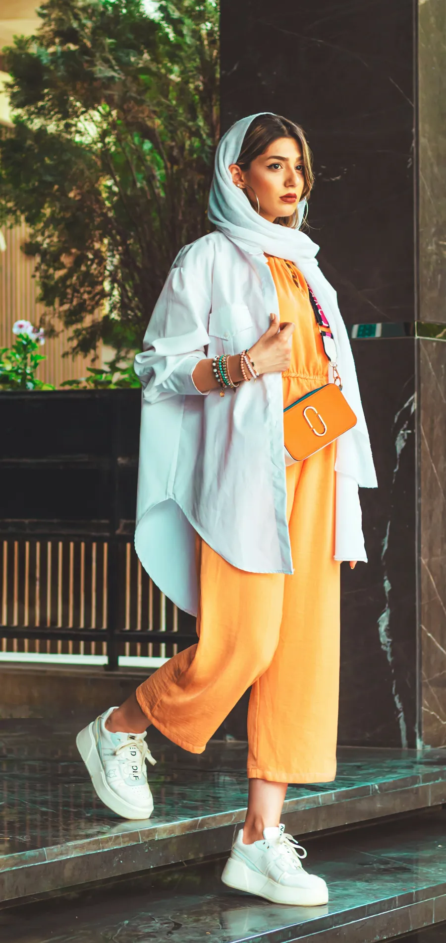 A seller in a cream knit top, light wide-leg jeans and a woven bag, filmed on a Dubai street at golden hour